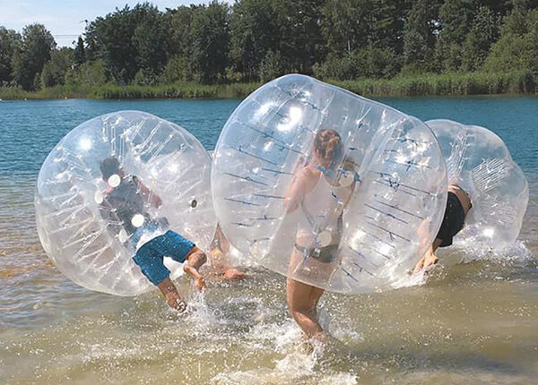 Jugendliche mit Bubble Soccer Ausrüstung springen in den Bernsteinsee