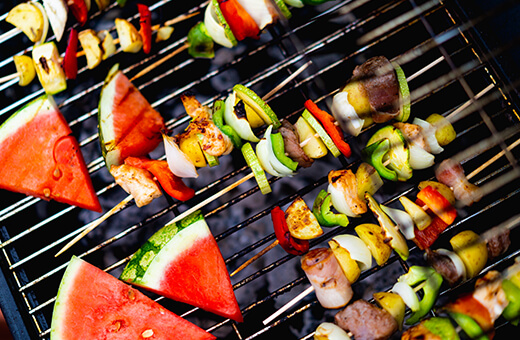 Grillspieße und Melonen auf dem Grillrost